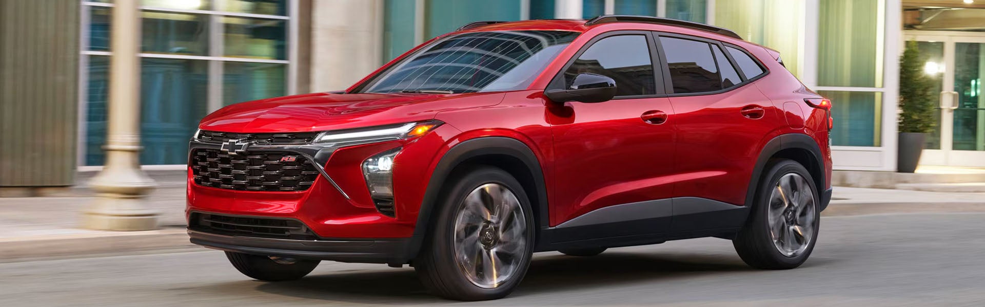 Red Chevrolet Trax driving past modern city buildings
